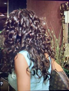 a woman with long curly hair standing in front of a mirror