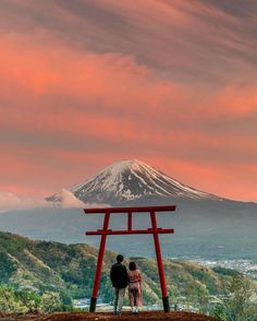 two people standing in front of a red chair with a mountain in the back ground