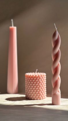 two candles are sitting on the table next to each other and one candle is pink