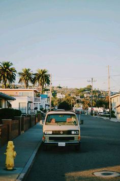 a van is driving down the street in front of a yellow fire hydrant and palm trees