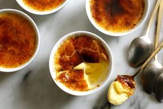 four bowls filled with food next to spoons on a marble counter top and utensils