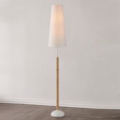 a floor lamp with a white shade on the base and a wooden stick in front of it