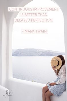 a woman wearing a straw hat sitting on top of a white wall next to a window