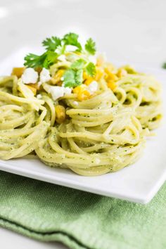 a white plate topped with pasta and garnished with cilantro, corn, and feta cheese