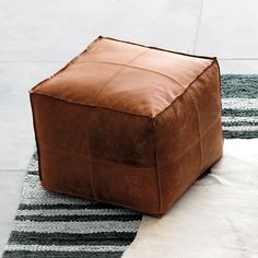 a square leather ottoman sitting on top of a rug