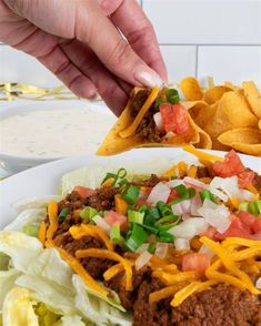 a person is holding a tortilla chip over a plate of taco salad