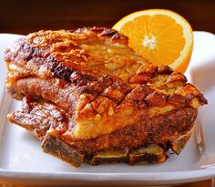 two pieces of meat sitting on top of a white plate next to an orange slice