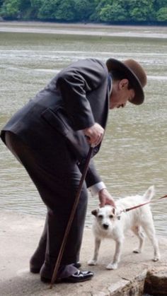 a man in a suit and hat is petting a white dog on a leash