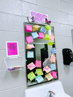 a mirror with sticky notes attached to it in a public bathroom stall that is decorated with pink, yellow and green post - it notes