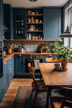 a kitchen with blue cabinets and wooden table in the center, surrounded by potted plants