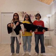 three girls standing in a room with one holding a large object and the other wearing sunglasses