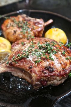 two pieces of meat on a plate with lemons and rosemary garnishes