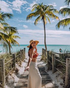 a woman in a straw hat is walking down the stairs to the beach with palm trees