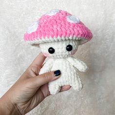 a hand holding a small crocheted stuffed animal with a pink and white mushroom on it's head