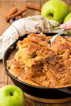 a person spooning some food out of a skillet with apples in the background