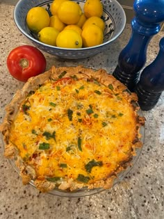 a pie sitting on top of a kitchen counter next to bowls of lemons and tomatoes