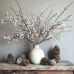 a white vase sitting on top of a wooden table filled with pine cones and branches