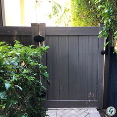 a wooden gate in the middle of a brick walkway between two bushes and a house