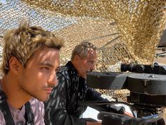 two men sitting next to each other on a motorcycle with a camera in front of them