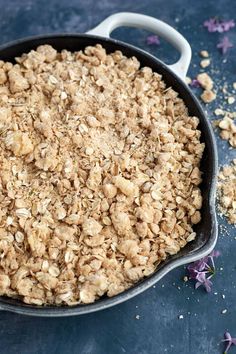 a pan filled with oatmeal sitting on top of a blue counter next to purple flowers