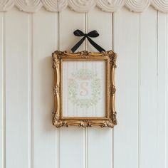 a gold frame hanging on the wall with a black bow