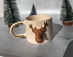 a ceramic mug with a deer head on it and three small trees in the background