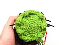 a crocheted green object being held by someone's hand on a white background