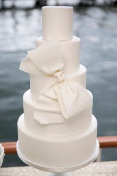 a three tiered white wedding cake with a large bow on top