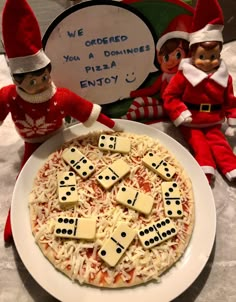 two elfs are sitting next to a pizza with dominos on it