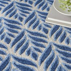 a blue and white rug with a plant in a vase on the floor next to it