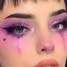 a close up of a woman with purple makeup and hearts on her cheek, looking at the camera