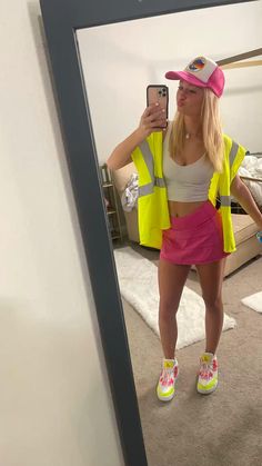 a woman taking a selfie in front of a mirror wearing yellow vest and pink hat