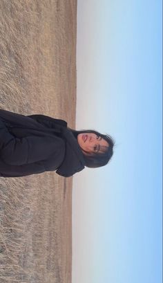 a man standing in front of the ocean with his head tilted to the side wearing a black jacket