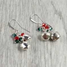 two silver bells with red, green and white beads are on the table next to each other