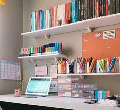 a laptop computer sitting on top of a desk next to a shelf filled with books