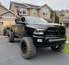 a large black truck parked in front of a house with two men standing on top of it