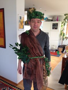 a man wearing a scarf with plants on his head standing in a living room next to a rug