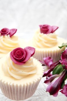 three cupcakes with white frosting and pink flowers on a glass platter