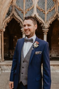 a man in a blue suit and bow tie standing next to an old church door