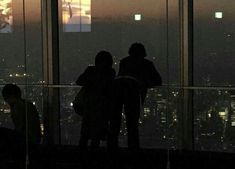 people are standing in front of the window looking at the city lights and skyscrapers