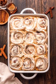 cinnamon rolls with cream cheese frosting in a white baking dish on a wooden table