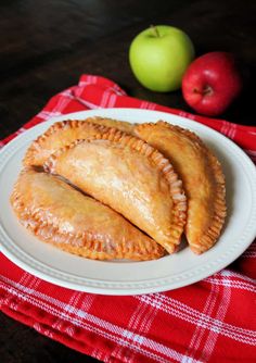 three pastries on a white plate next to an apple and red checkered napkin