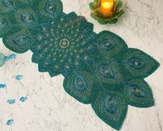 a green doily with peacock feathers on it next to a candle