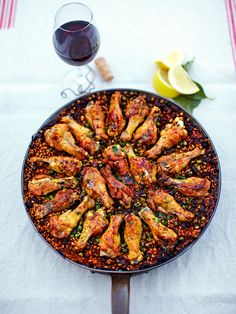 a pan filled with chicken wings next to a glass of wine and lemon wedges