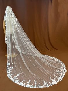 a wedding veil with white flowers on the bottom is displayed in front of a brown backdrop