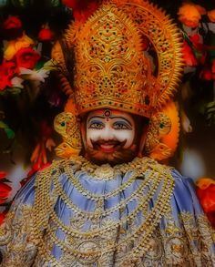 an elaborately decorated mask with flowers in the background and a man's face painted on it