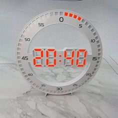 an alarm clock with red numbers in the middle on a white marble counter top next to a silver car