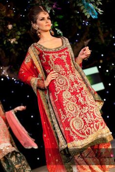 a woman in red and gold outfit walking down the runway with her hands on her hips