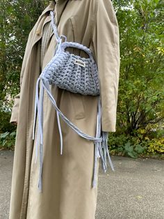 a woman wearing a trench coat and holding a crocheted purse