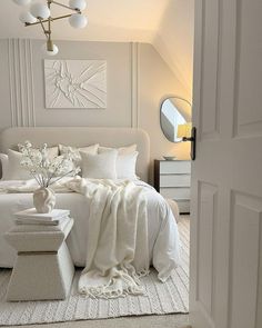 a white bed with pillows and blankets on top of it next to a mirror in a room